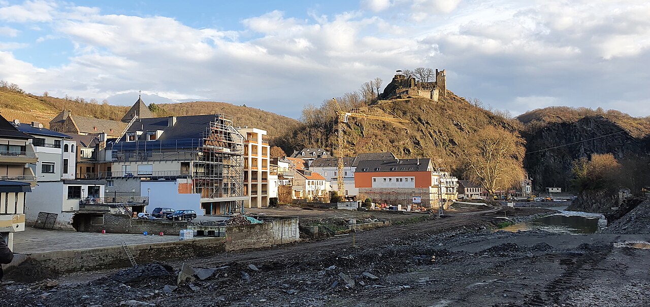 Zerstörtes Flussufer in Altenahr: Schutt, kahle Flächen und beschädigte Häuser, im Hintergrund eine Burgruine