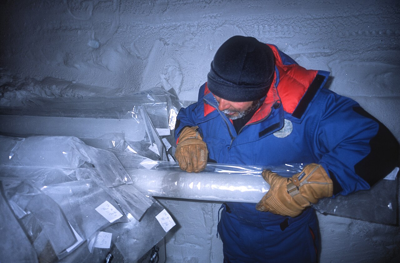 Ein Forscher in dicker Polarkleidung untersucht einen länglichen Eisbohrkern in einem Eislabor