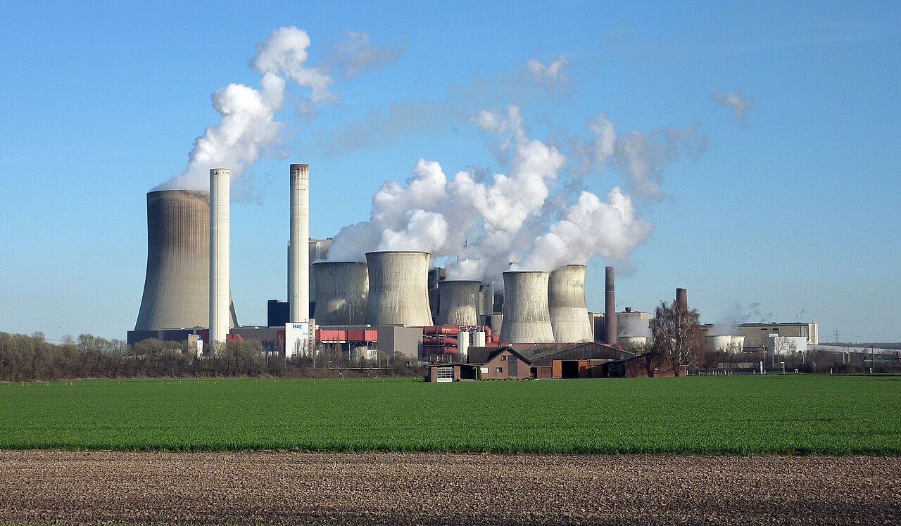 Braunkohlekraftwerk mit mehreren Kühltürmen und Schornsteinen, aus denen weiße Wolken aufsteigen